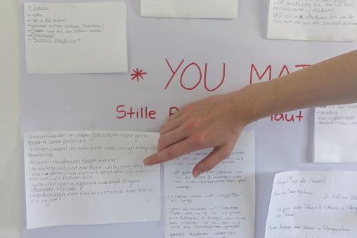 Eine Tafel mit vielen Zetteln, Ideen für Postkarten, Eine Hand zeigt auf einen Zettel